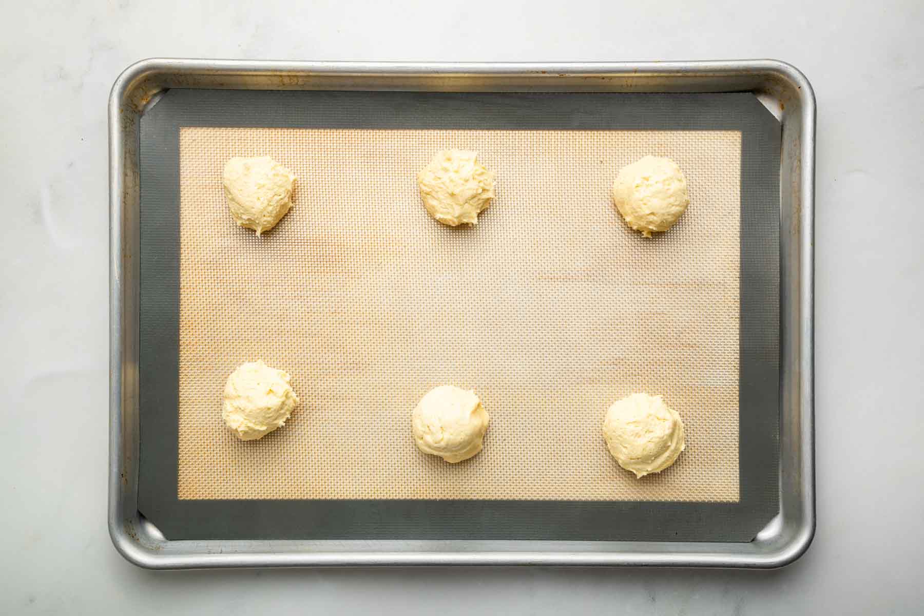 Six balls of Lofthouse cookie dough on a silicone lined baking sheet.
