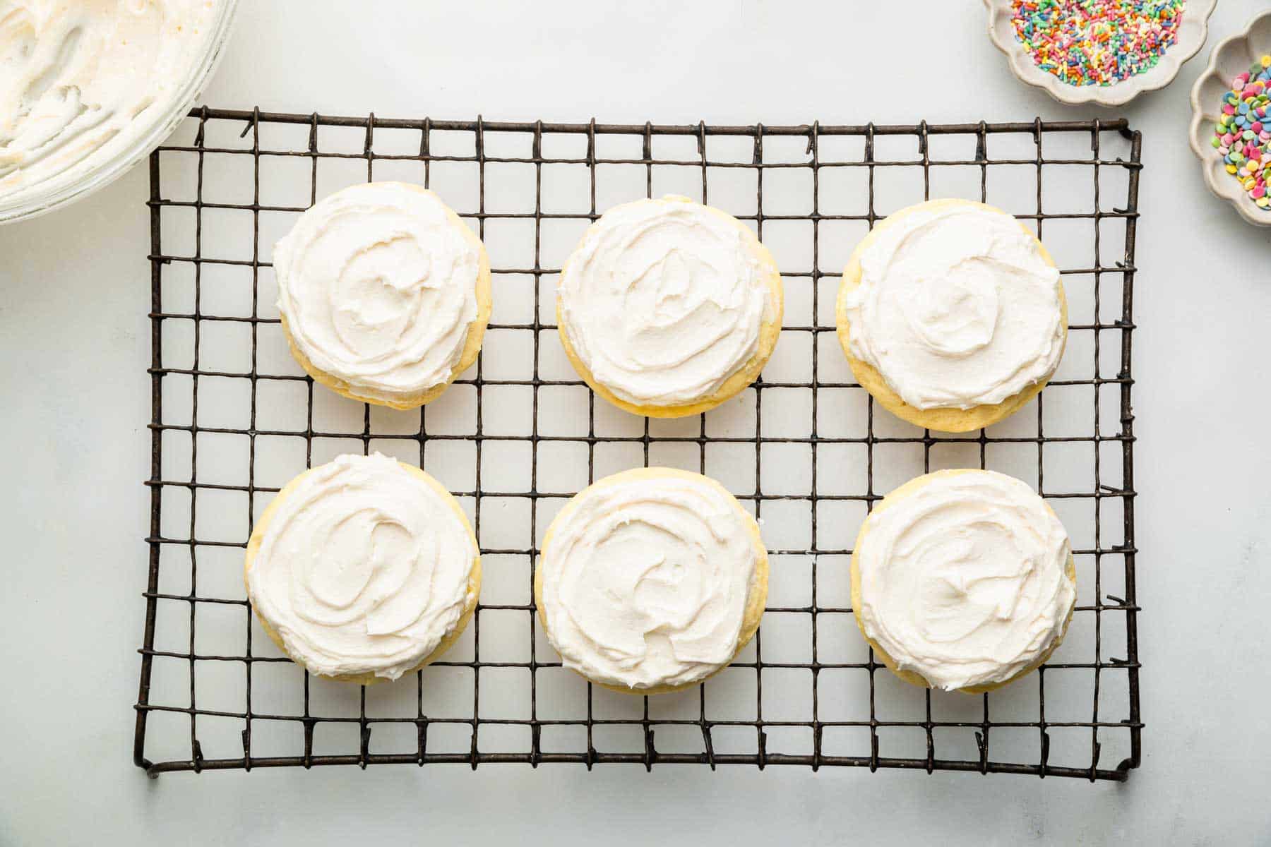 Six cookies on a wire rack frosting with white frosting.