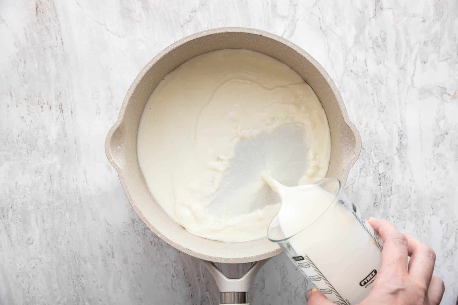 Hand pouring milk into a grey saucepan.