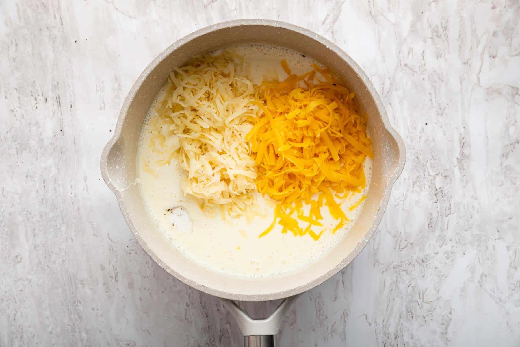 Two types of grated cheese in a saucepan with milk.