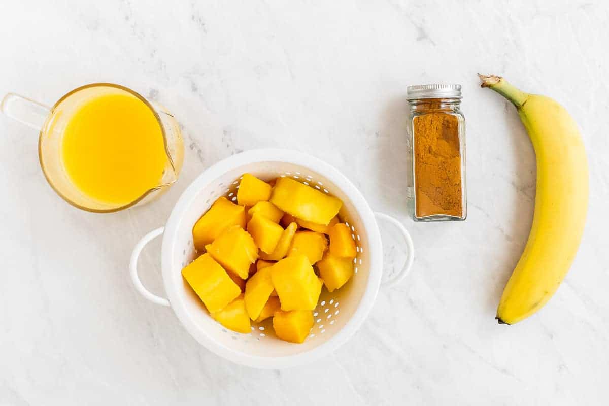 Orange juice, mango, turmeric and banana on white table.
