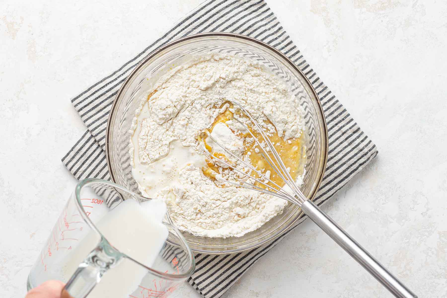 Pouring milk into cupcake batter in bowl.