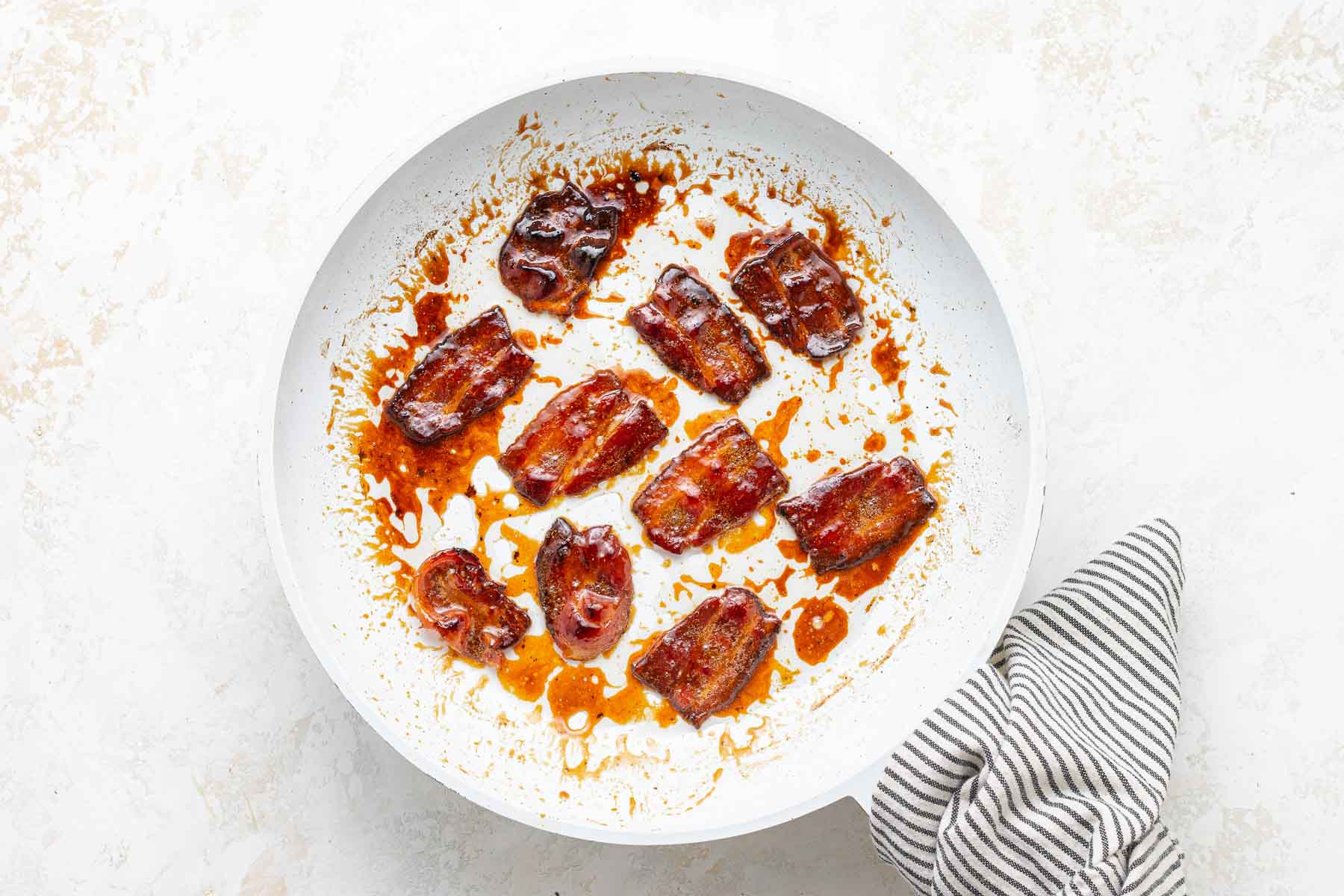 Bacon cooked in white skillet with maple syrup on top.