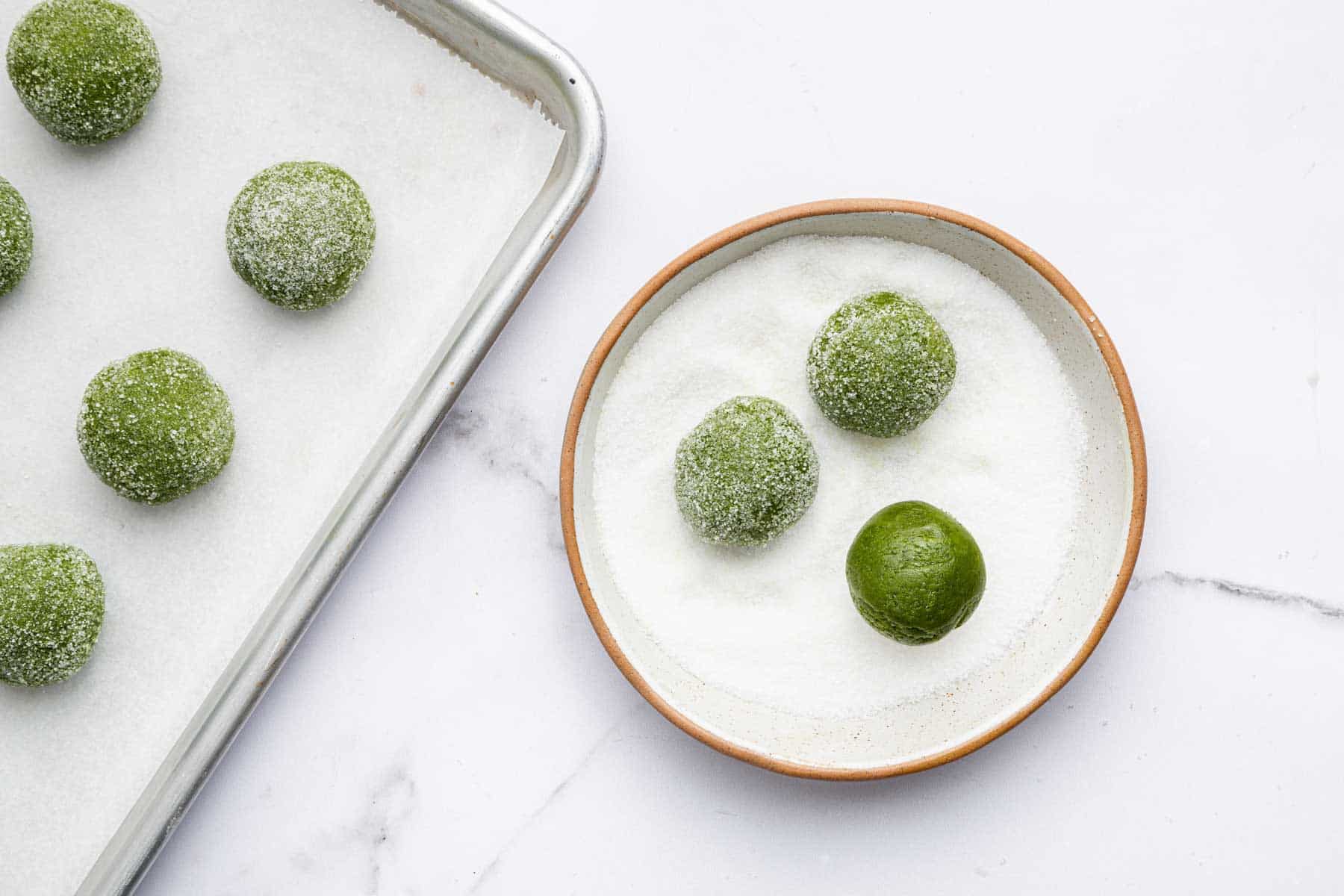 Little balls of green dough being rolled in sugar.
