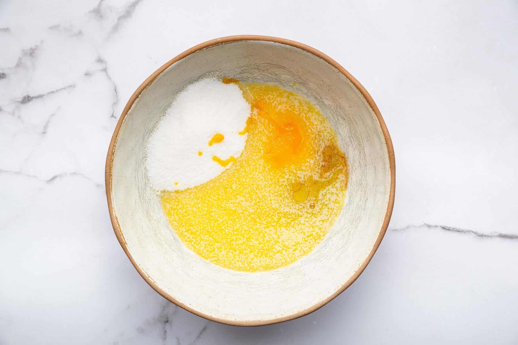 White bowl with melted butter, sugar, egg and vanilla inside.