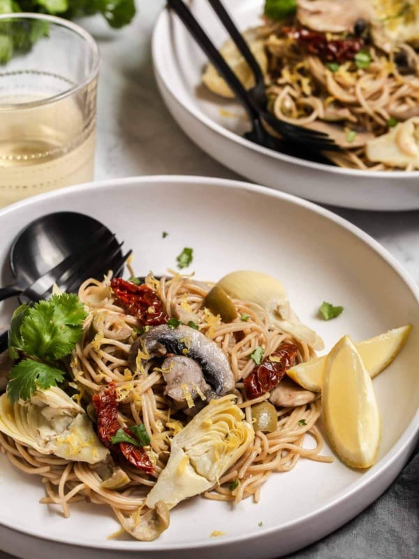 Pasta on plate with mushrooms, sun-dried tomatoes and lemon slices.