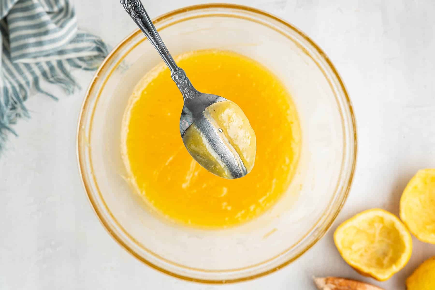 Metal spoon dipped in microwave lemn curd with streak through it.