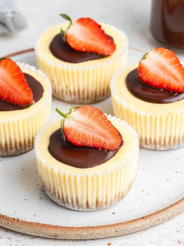 Vertical photo of four mini cheesecakes in muffin liners with a half strawberry on top.
