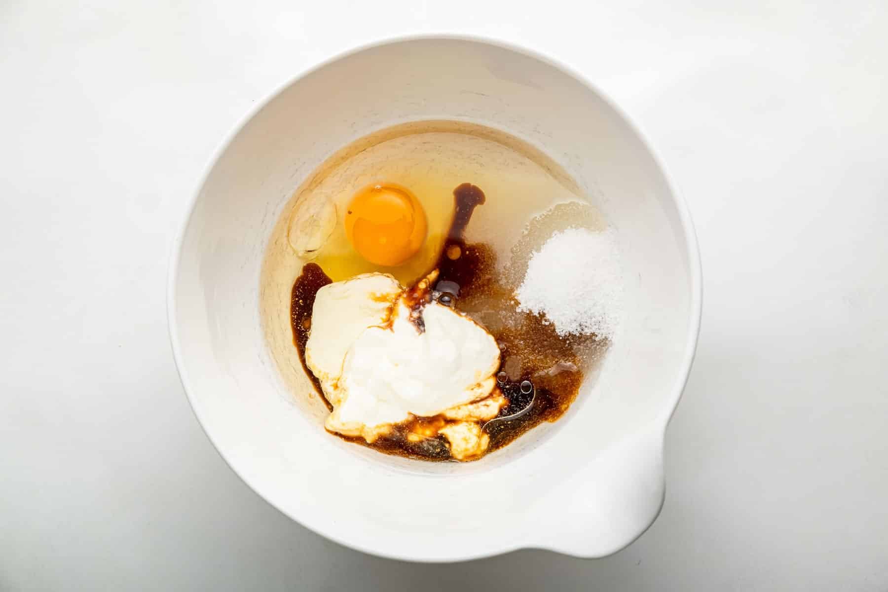 Egg, sugar, vanilla and sour cream in white bowl.