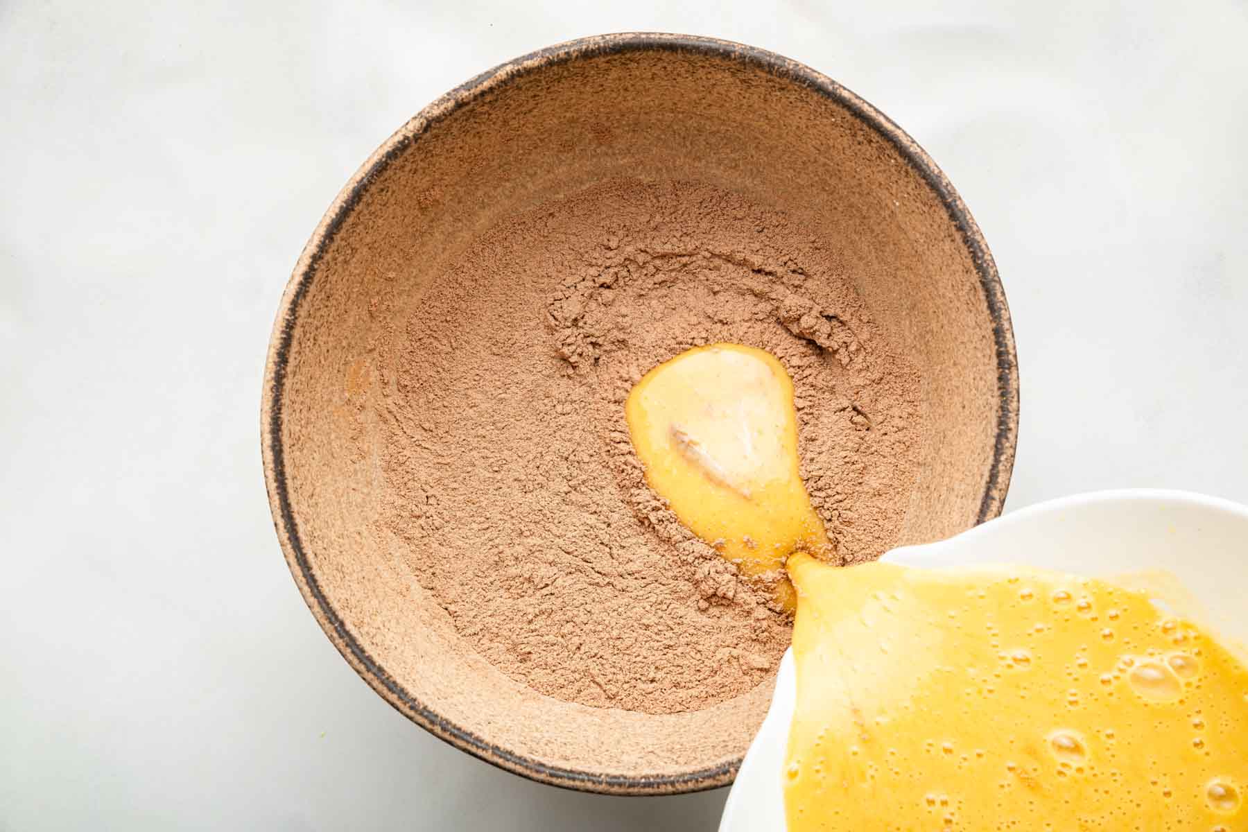 Pouring yellow liquid into brown powder in brown bowl.