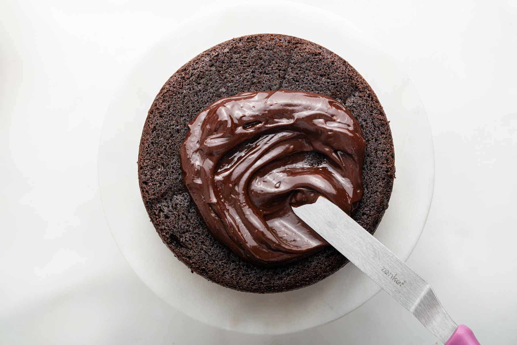 Spatula spreading ganache on a small batch chocolate cake.