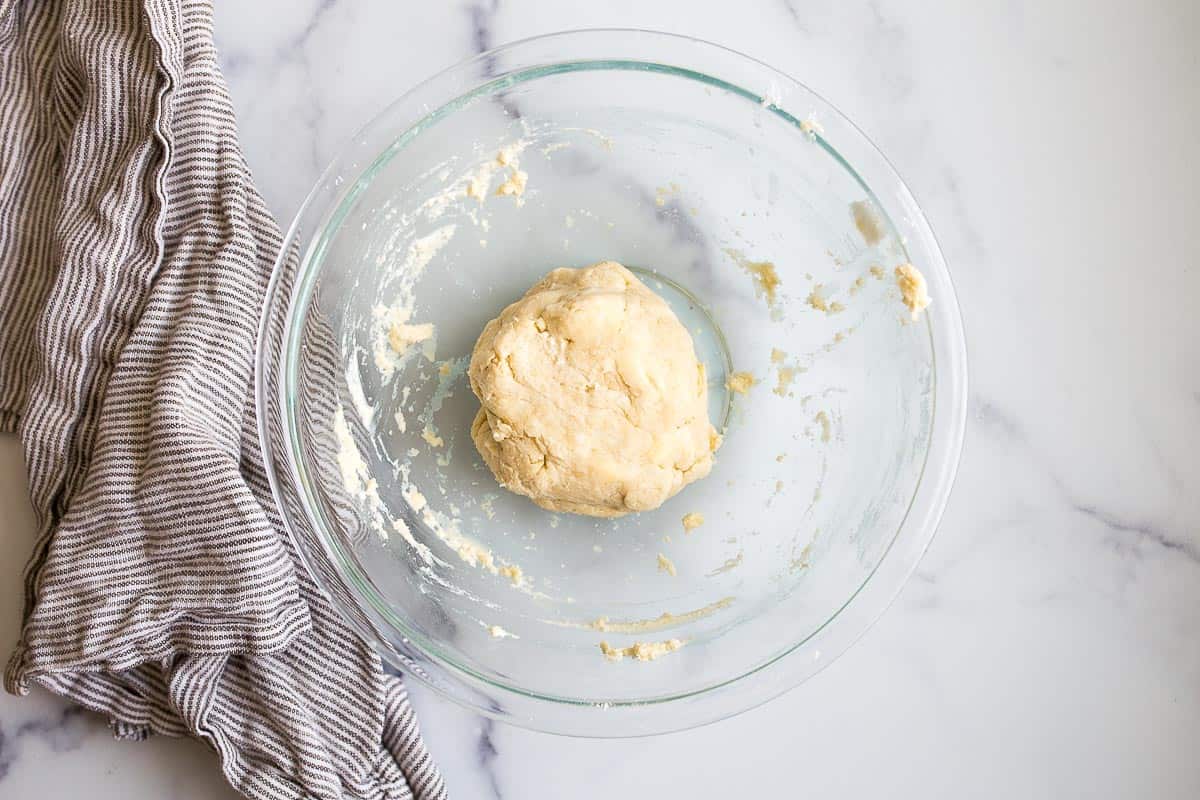 A ball of yellow dough with butter flecks in a clear glass bowl with striped napkin on the side.