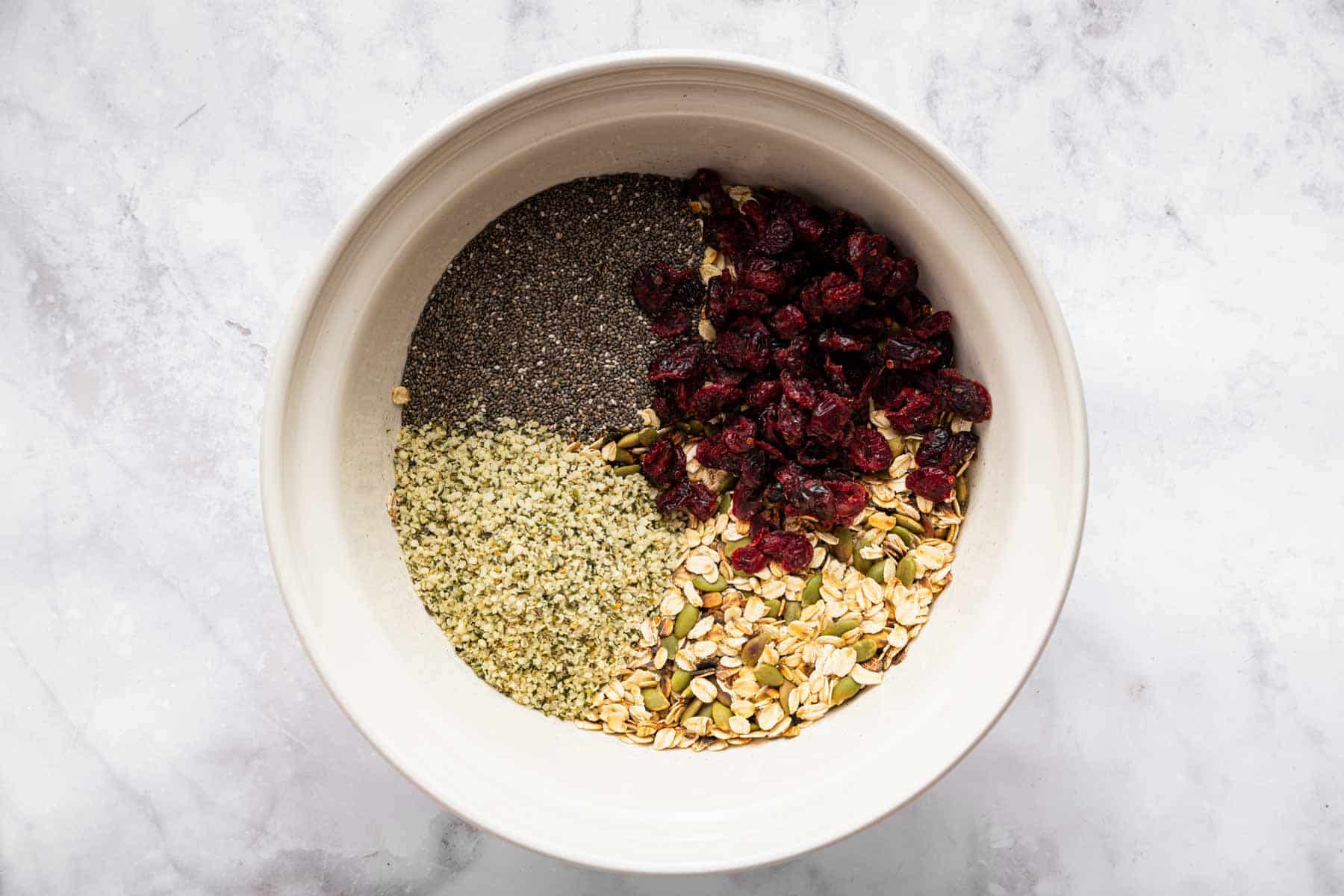 Large mixing bowl with cranberries, chia seeds, and hemp hearts with oats.