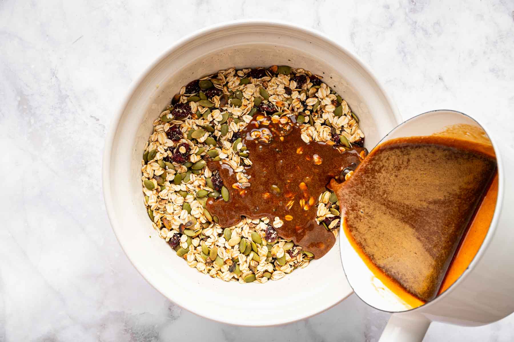 Brown liquid being poured on a oat and seed mixture.