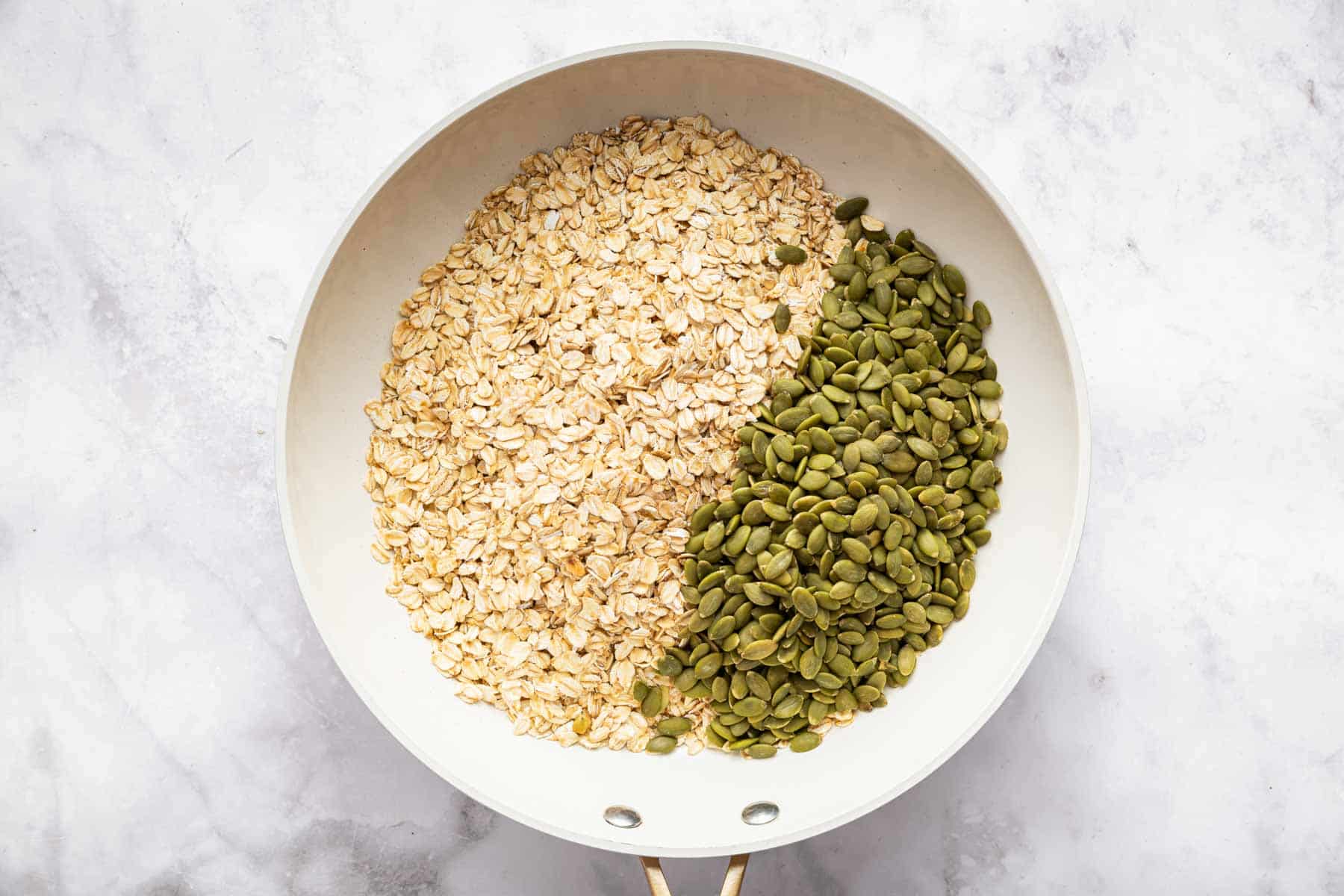 Rolled oats and pumpkin seeds in a white skillet.