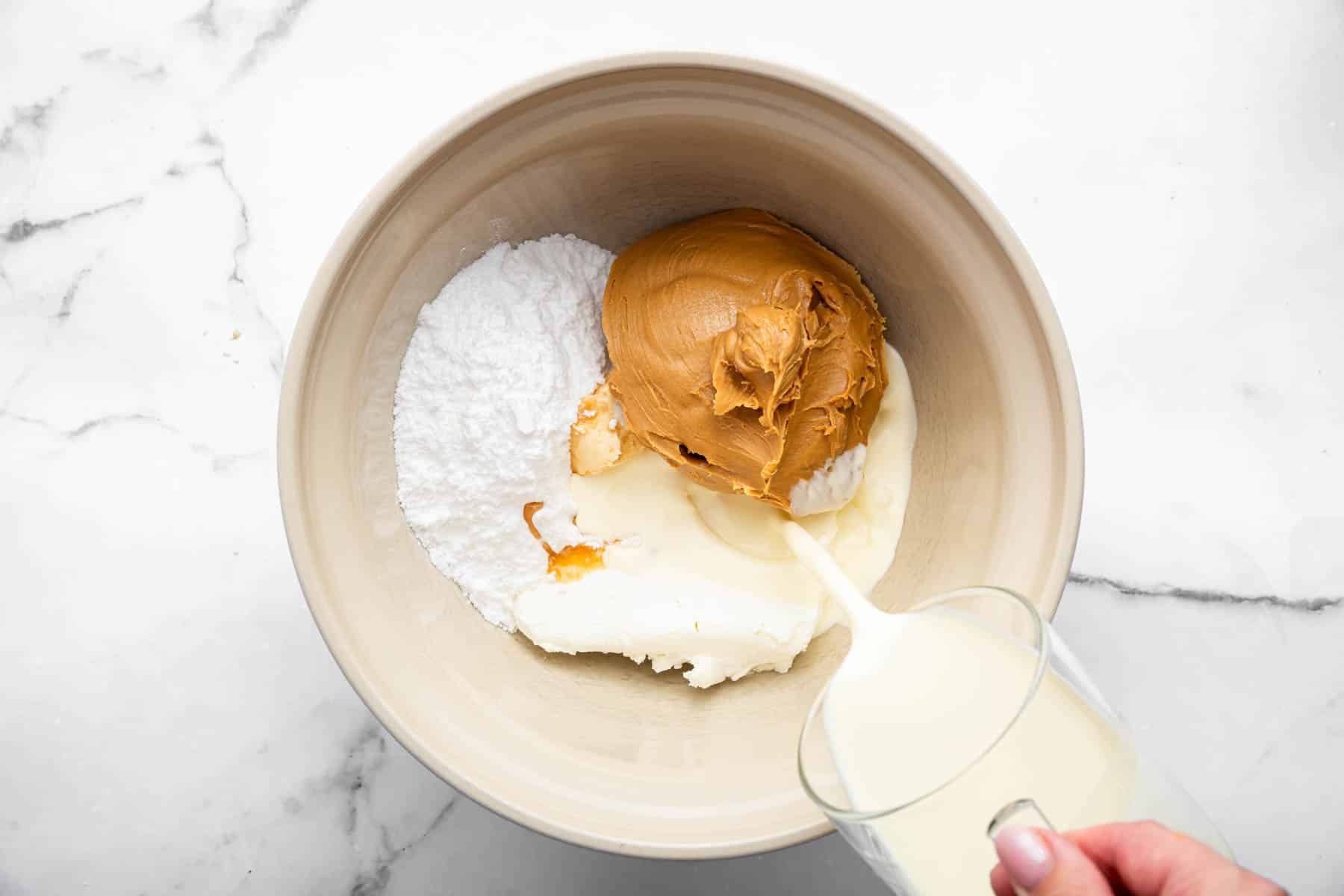 Bowl with baking ingredients and a hand pouring in cream.