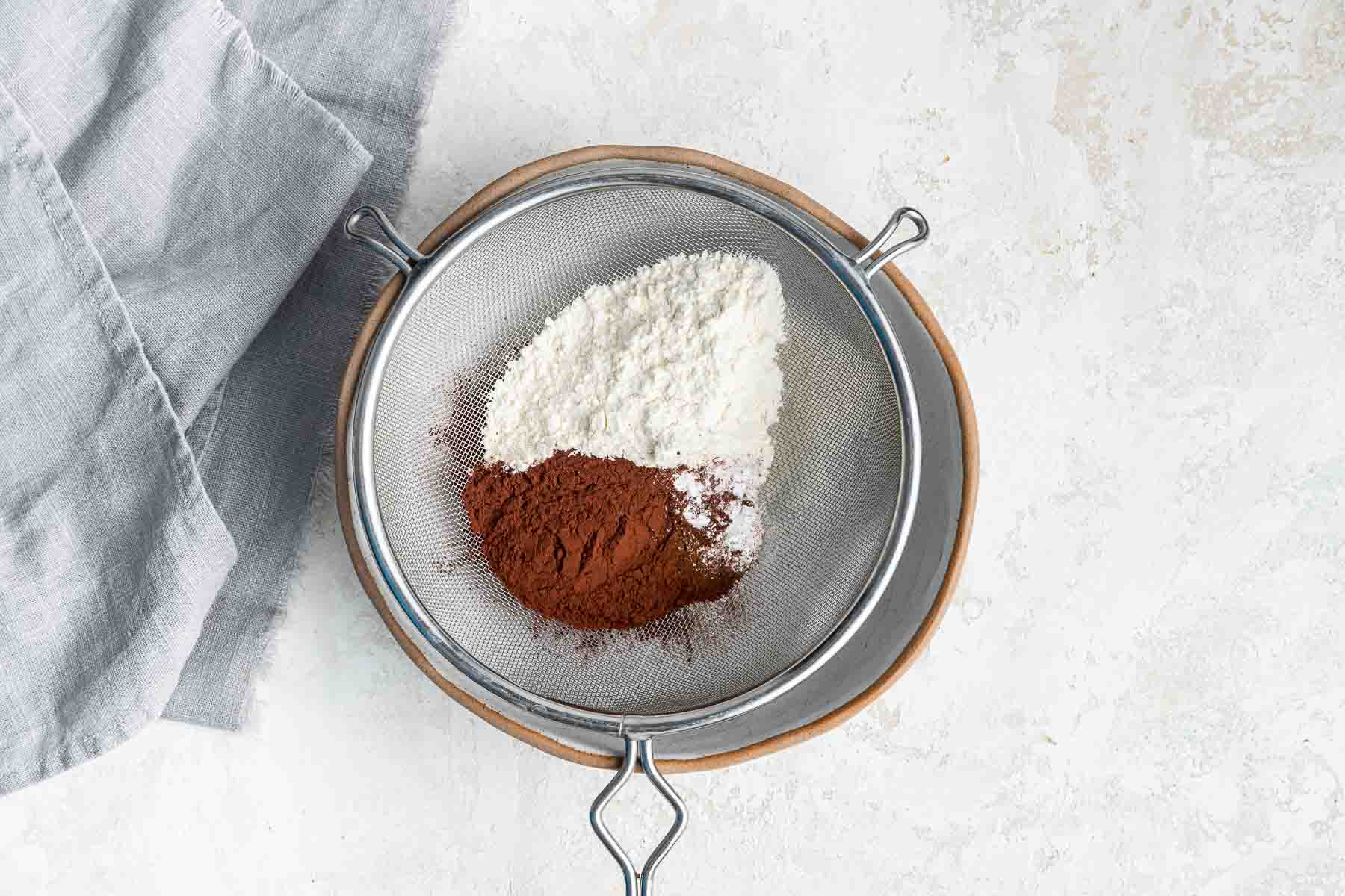 Bowl with sifter containing cocoa powder and flour.