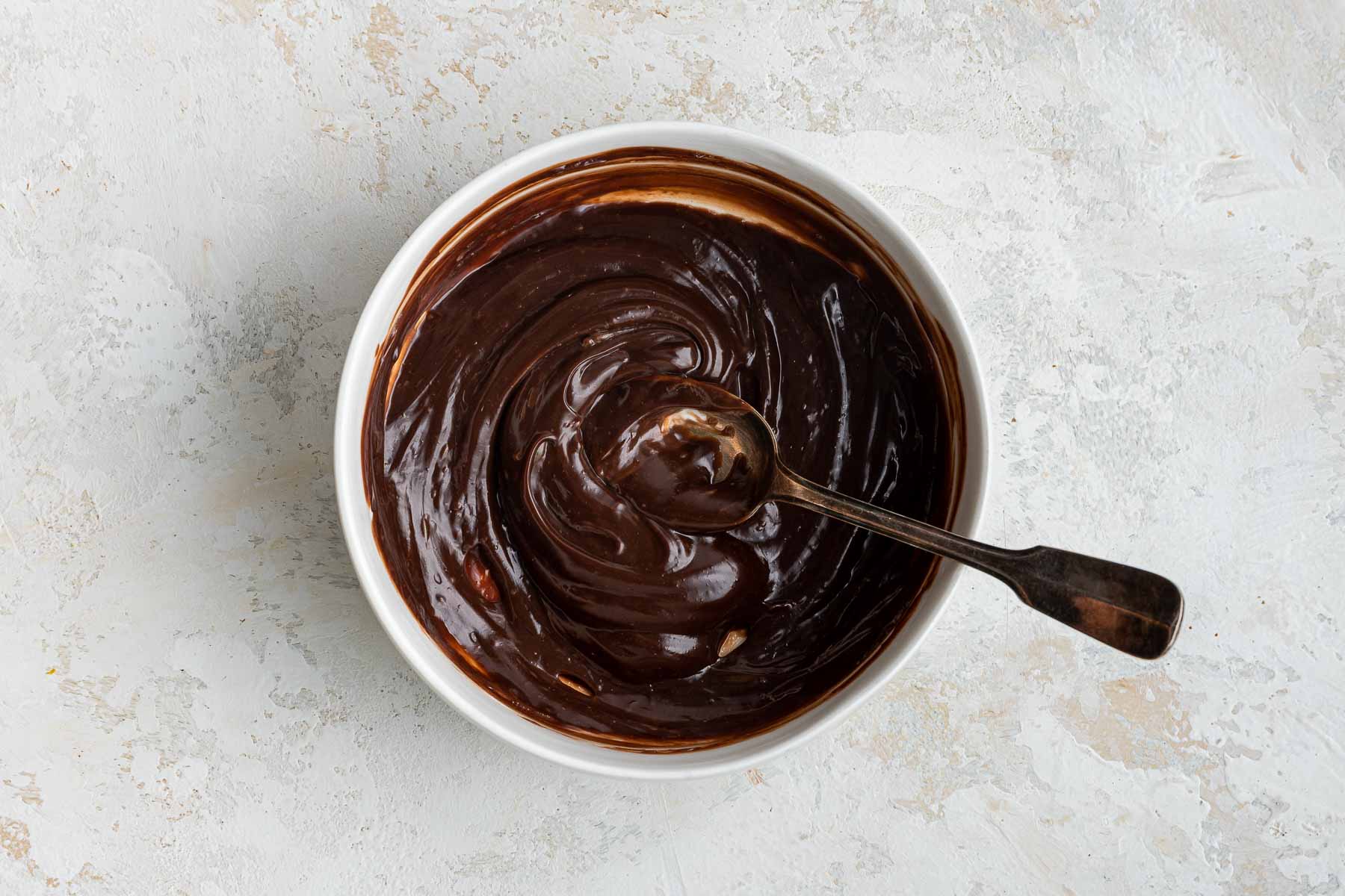 Nutella and sour cream stirred together in a white bowl with a spoon.