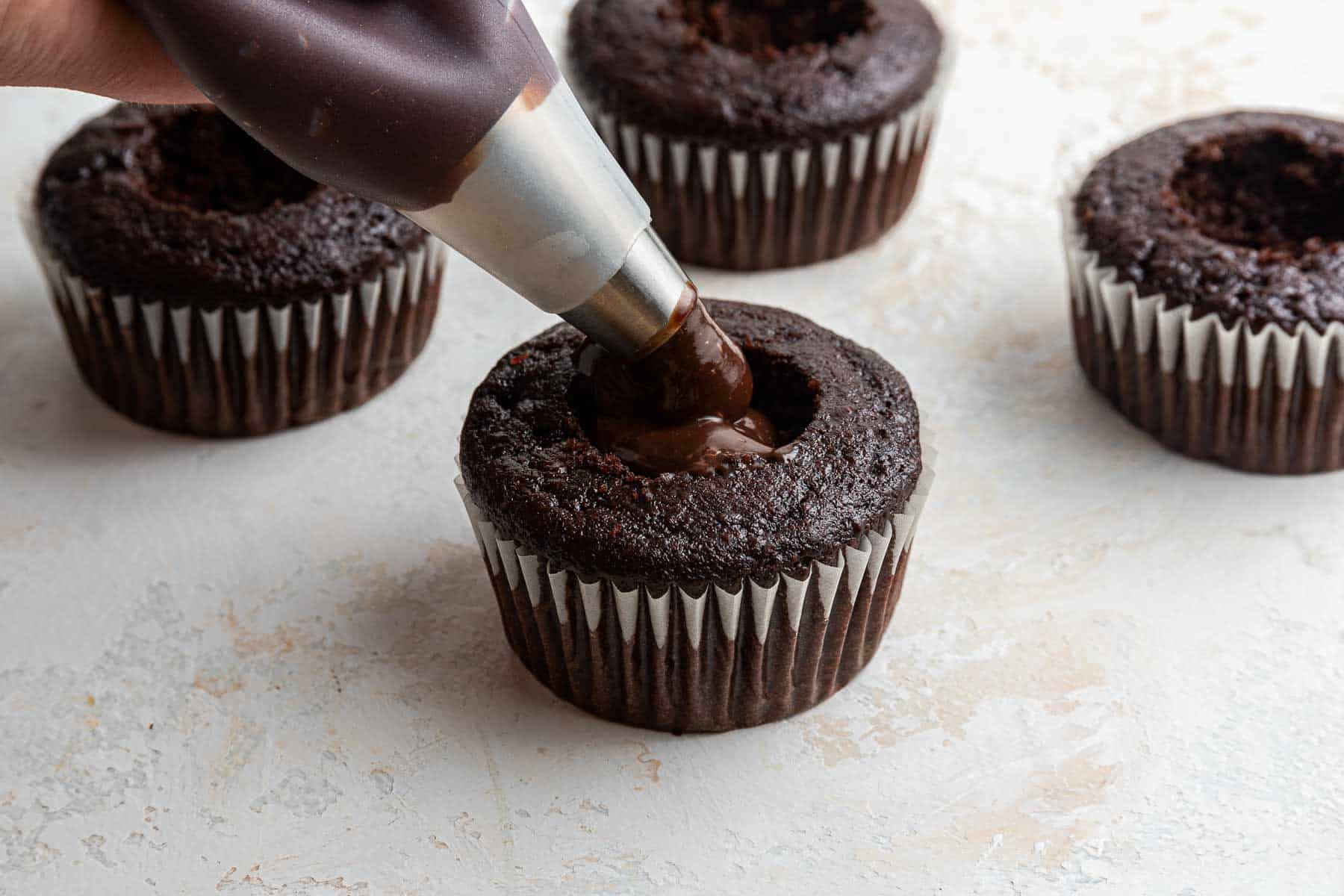 Pouring molten chocolate filling into a cake with a piping bag.