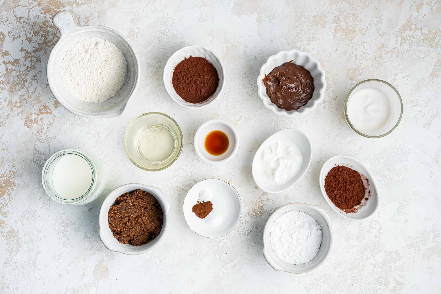 Small white bowls of ingredients for Nutella cupcakes on marble counter.
