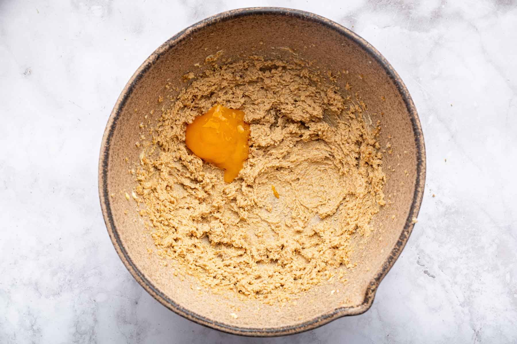 Whole egg yolk on top of creamy batter in brown bowl.