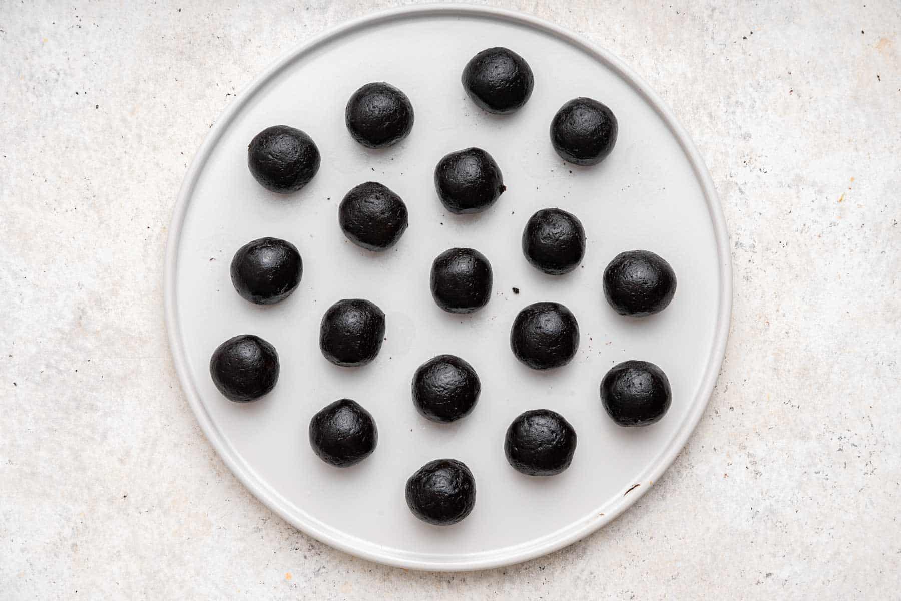 Round plate with 18 small black desserts on it.