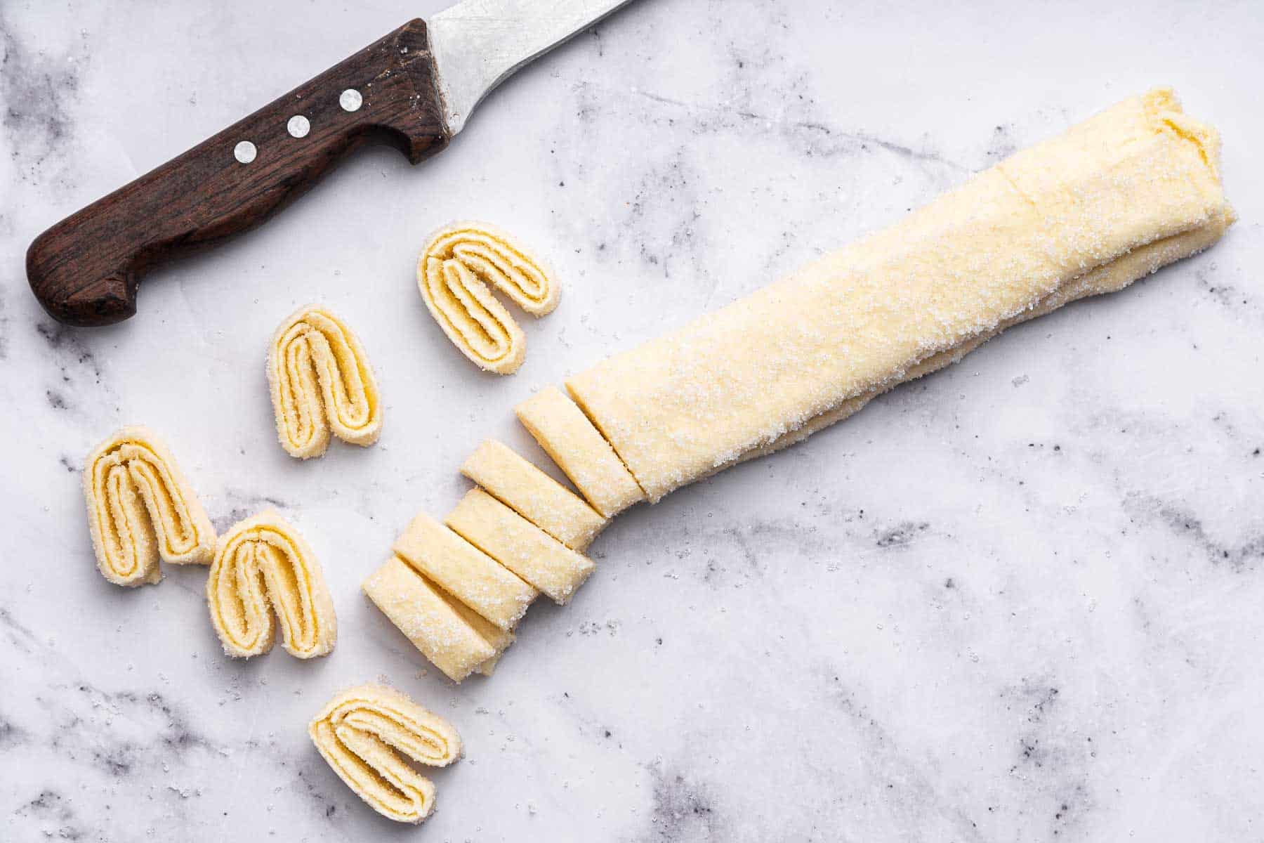 Knife cutting through pastry on marble board.
