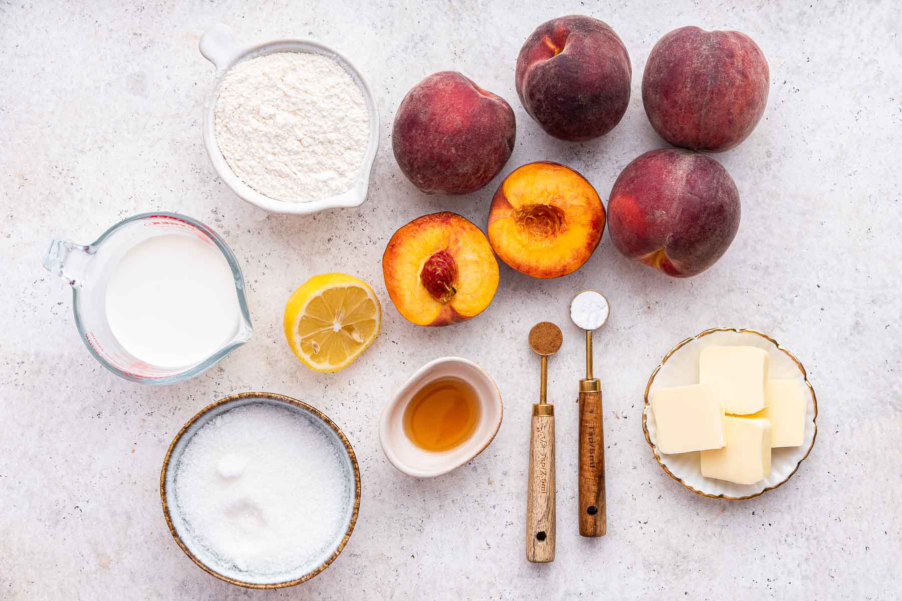 Sliced peaches and bowls of sugar, flour, lemon juice and vanilla on counter top.