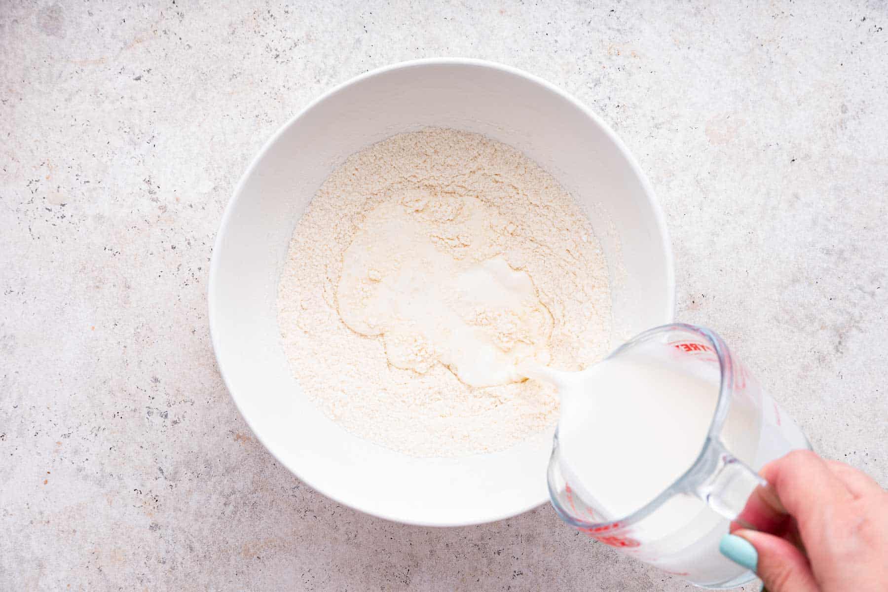 Pouring half and half into flour mixture in white bowl.