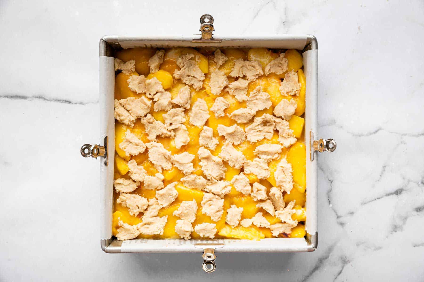 Square dessert with yellow fruit and dough bites sprinkled evenly on top.