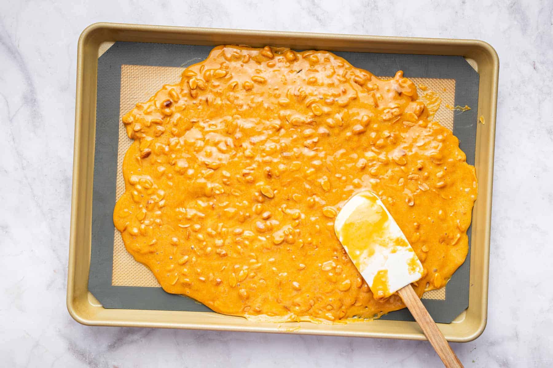 Peanut brittle spread on a baking sheet with a spatula.