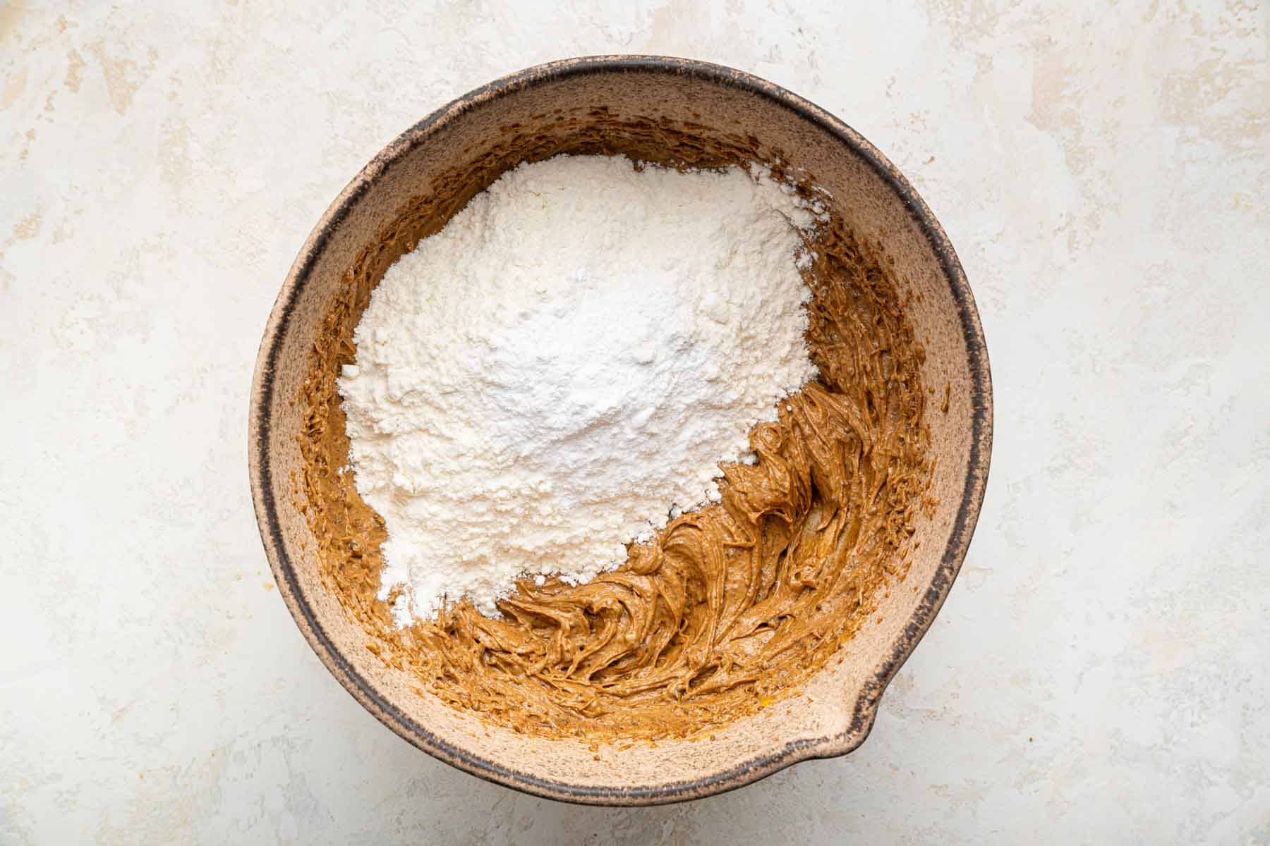 White flour on top of brown batter in brown bowl.