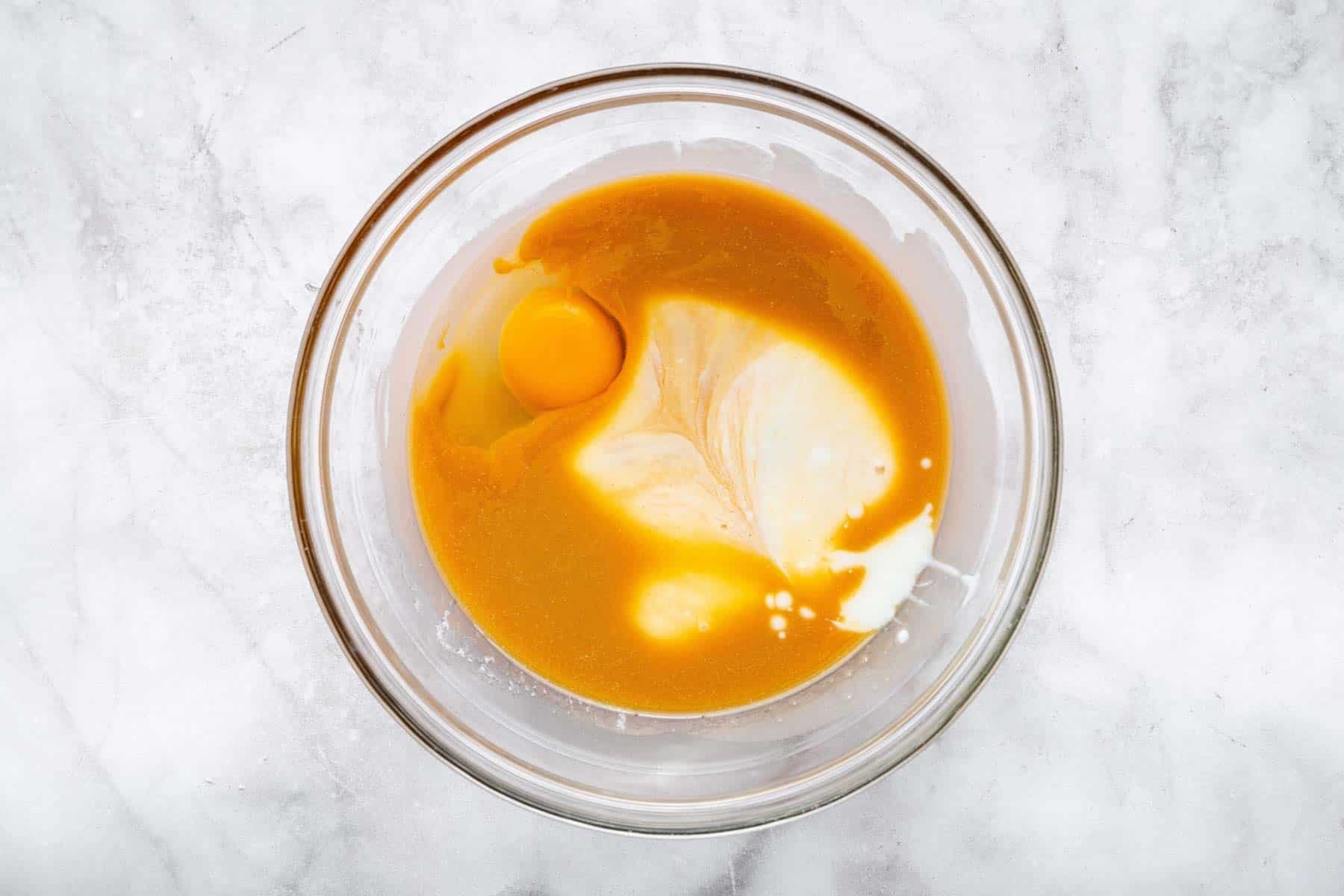 Clear glass bowl with melted brown liquid, egg and milk.