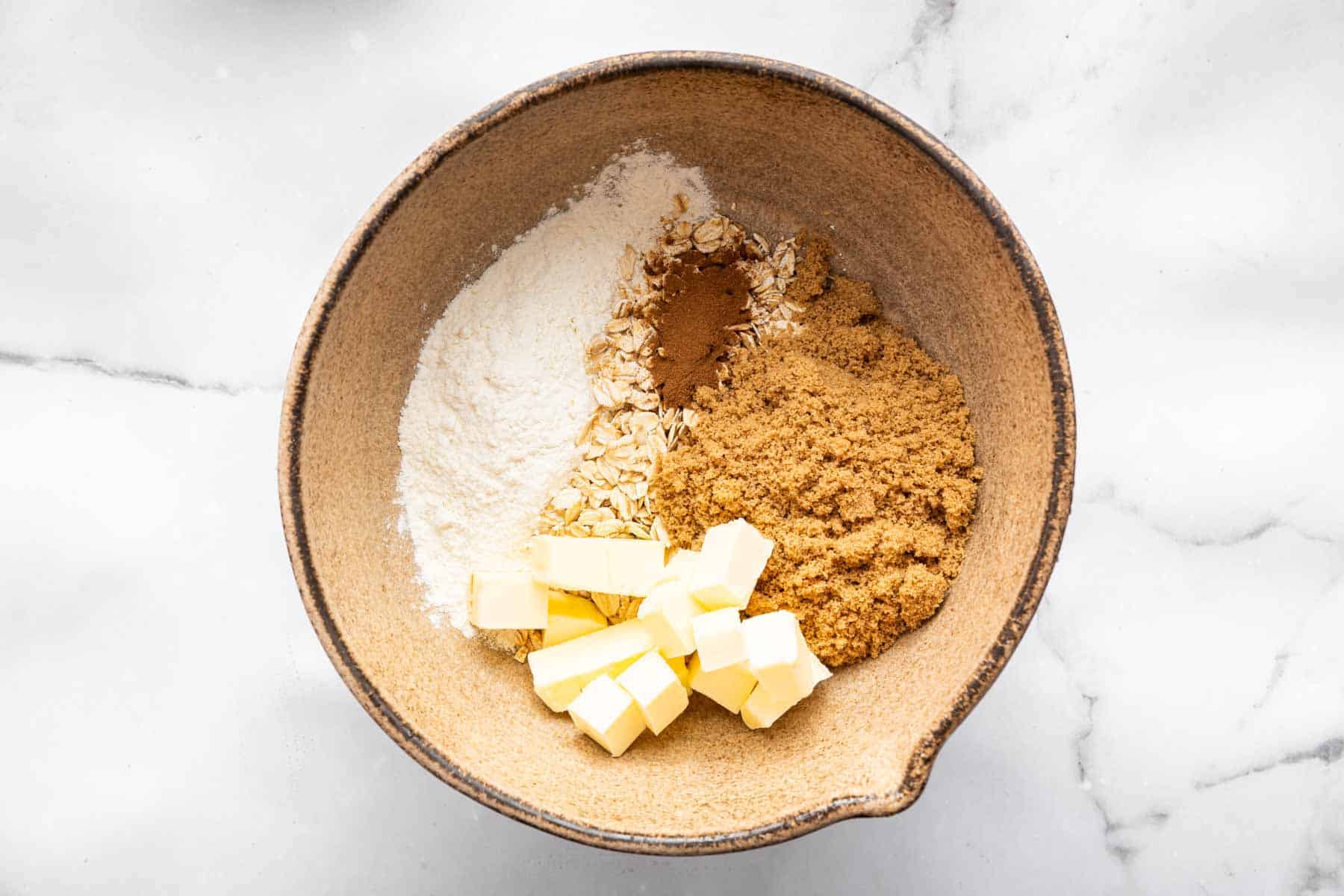 Bowl with brown sugar, diced butter, flour, oats, and brown spices.