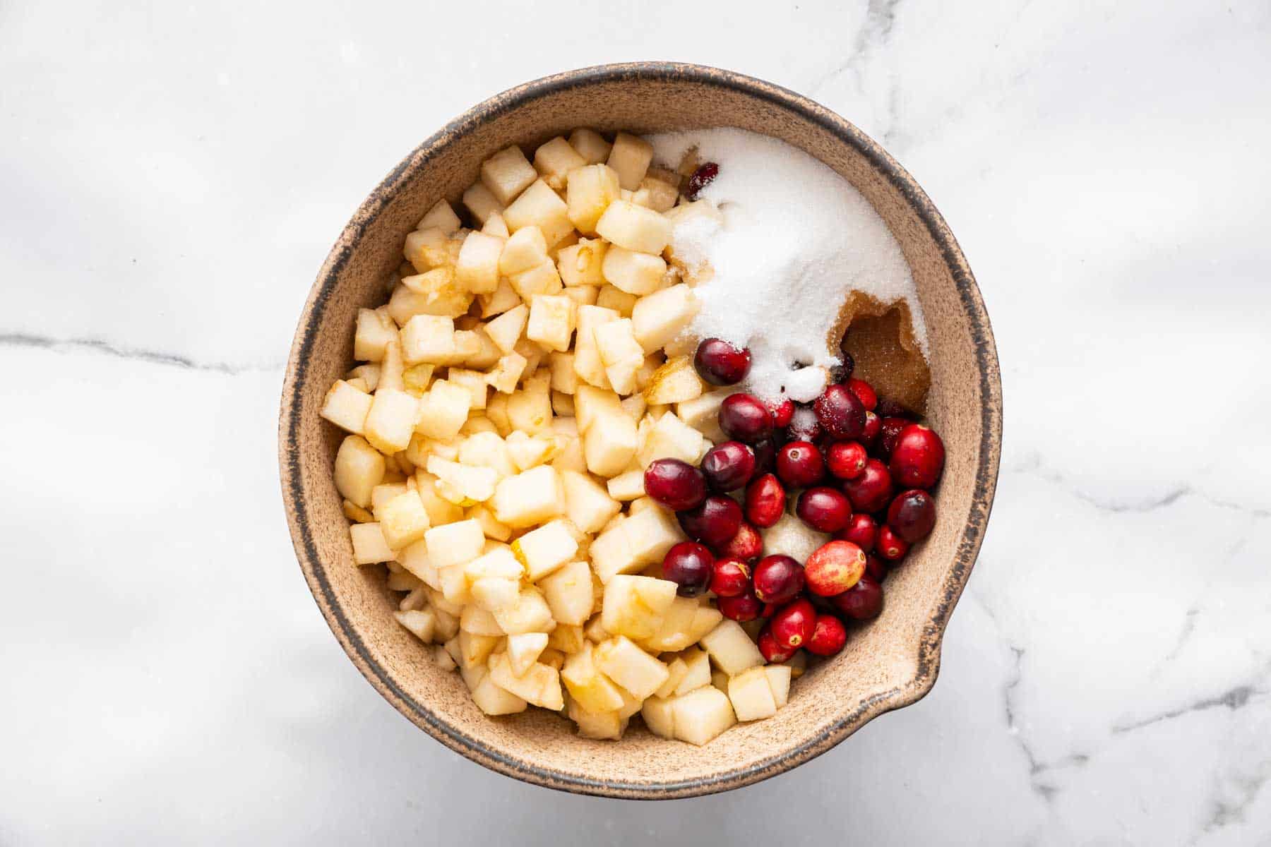 Brown bowl with diced white fruit and fresh cranberries inside.