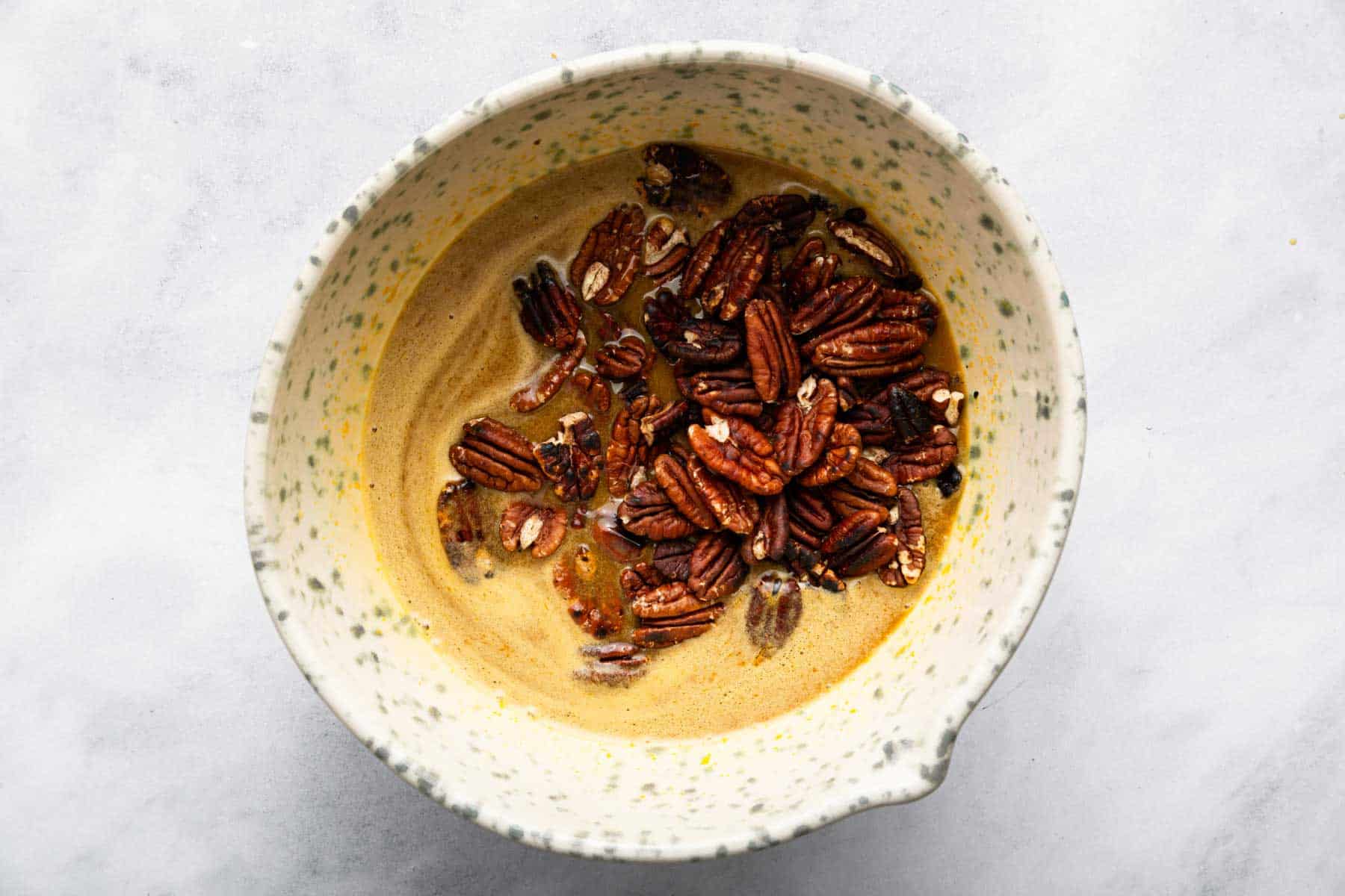 Tan batter in speckled bowl with whole nut halves on top.