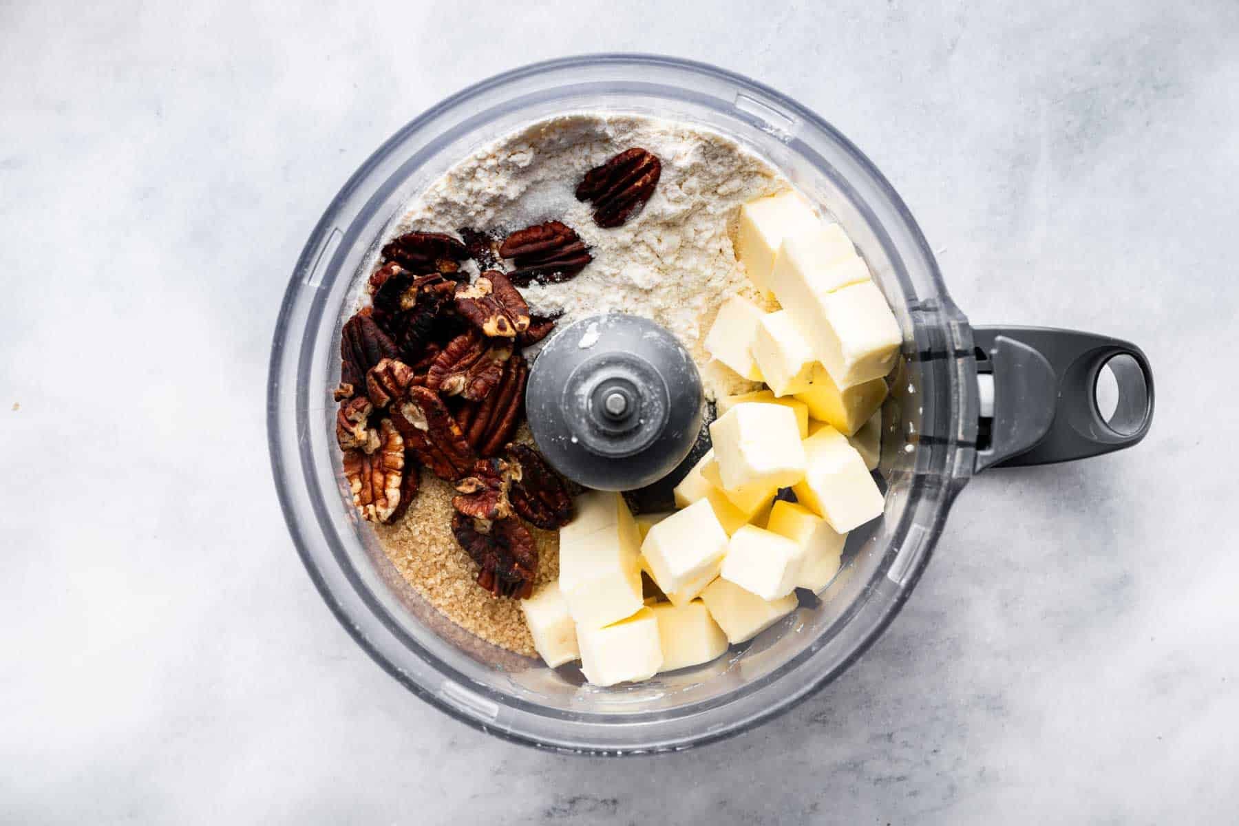 Food processor bowl with diced butter, flour, sugar, and pecan halves.