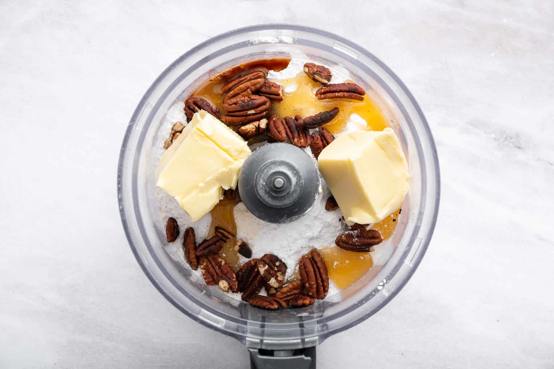 Food processor bowl with butter, nuts, and honey.