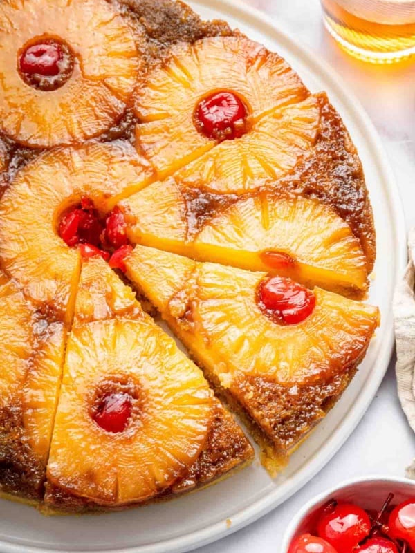 Vertical image of pineapple upside down cake with cherries in center.