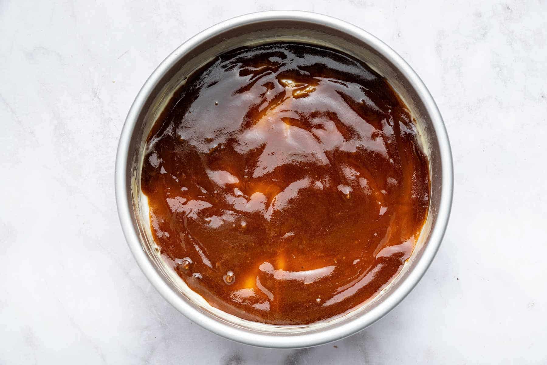 Brown caramel sauce in the bottom of a round pan.