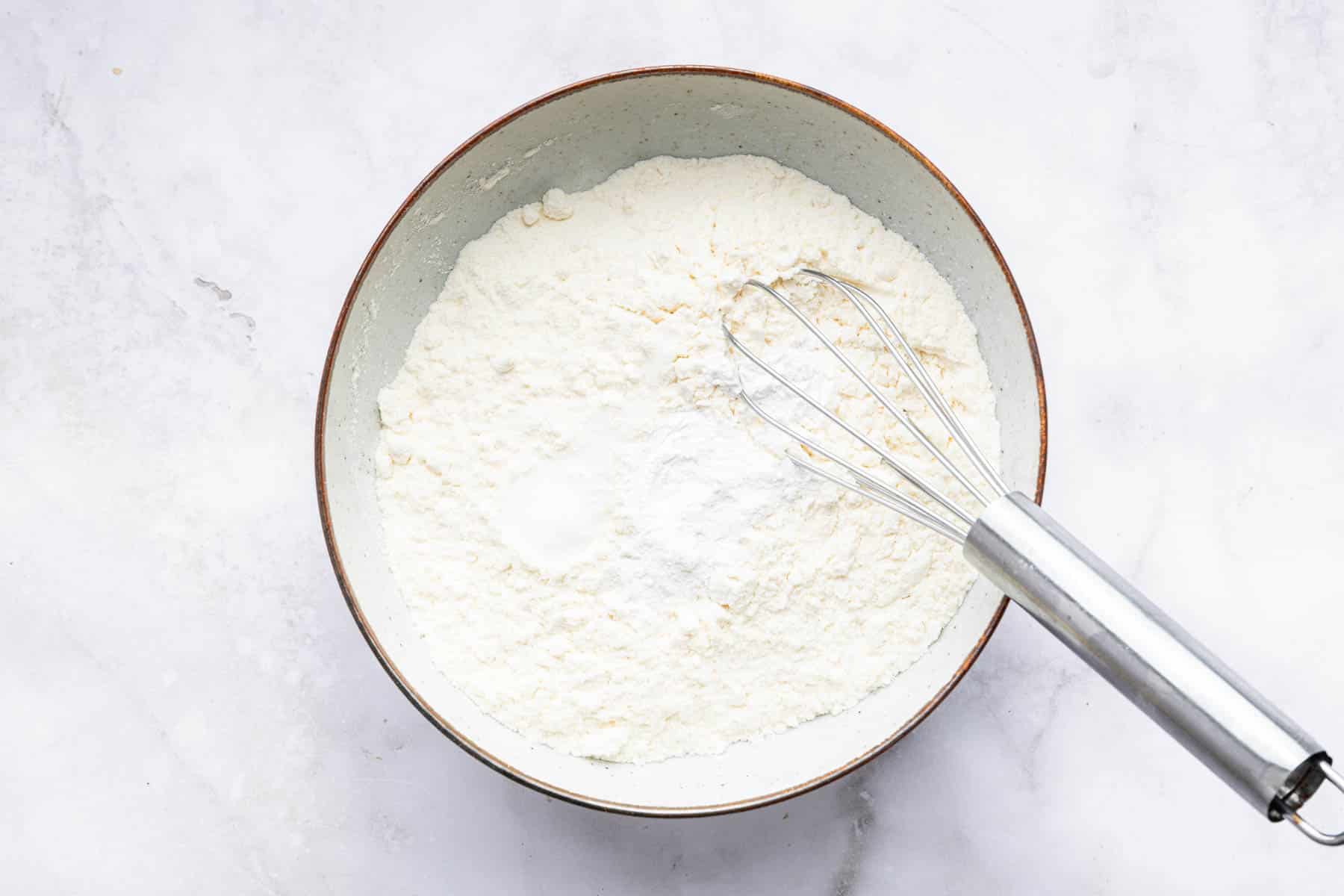 White bowl with white powders in it with a whisk.