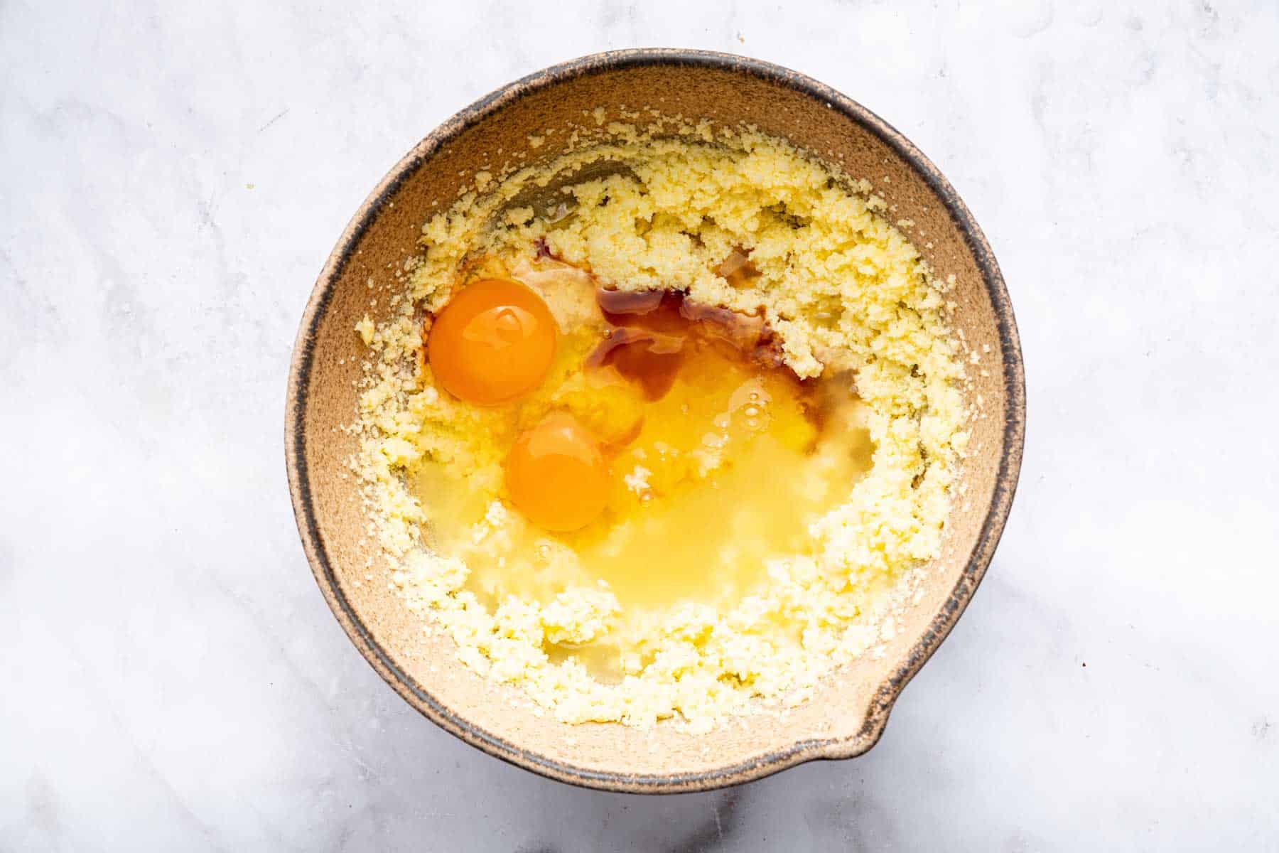 Bowl with yellow butter, eggs and vanilla splashed on top.