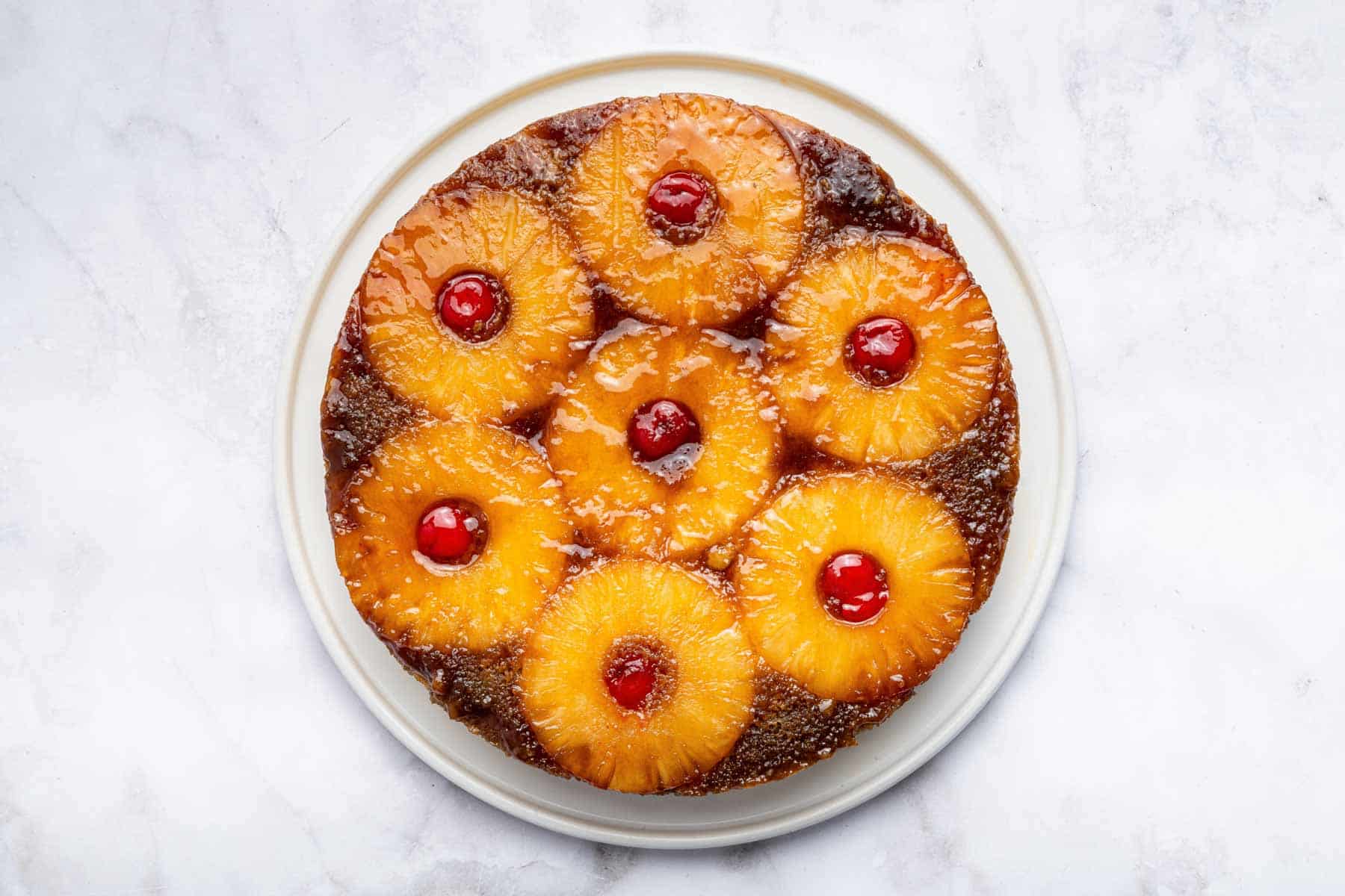 A pineapple upside down cake flipped over on a white plate for serving.