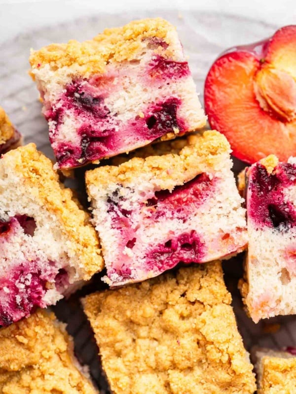 Slices of plum cake with streusel on a platte with a half plum nearby.