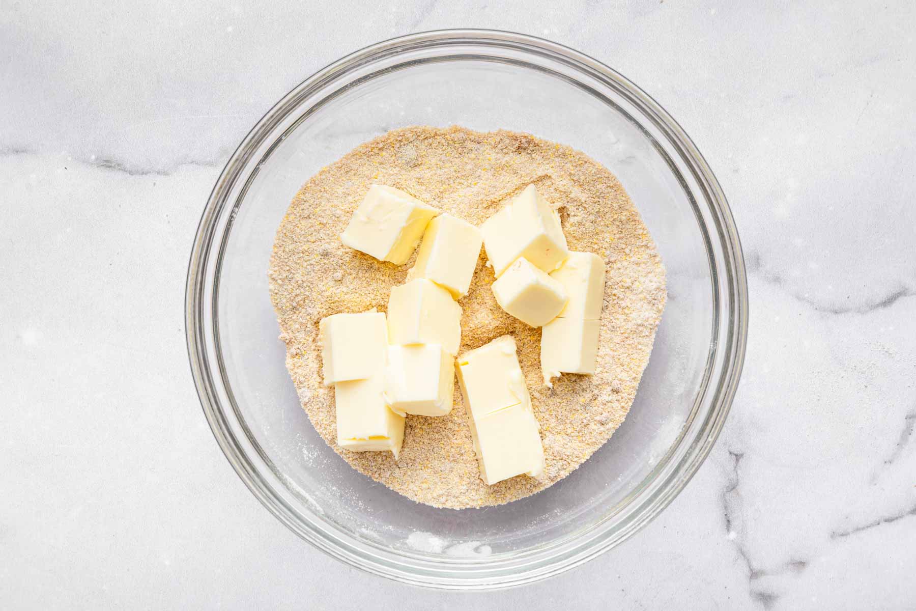 Cubes of butter over a sugar crumble mixture in bowl.