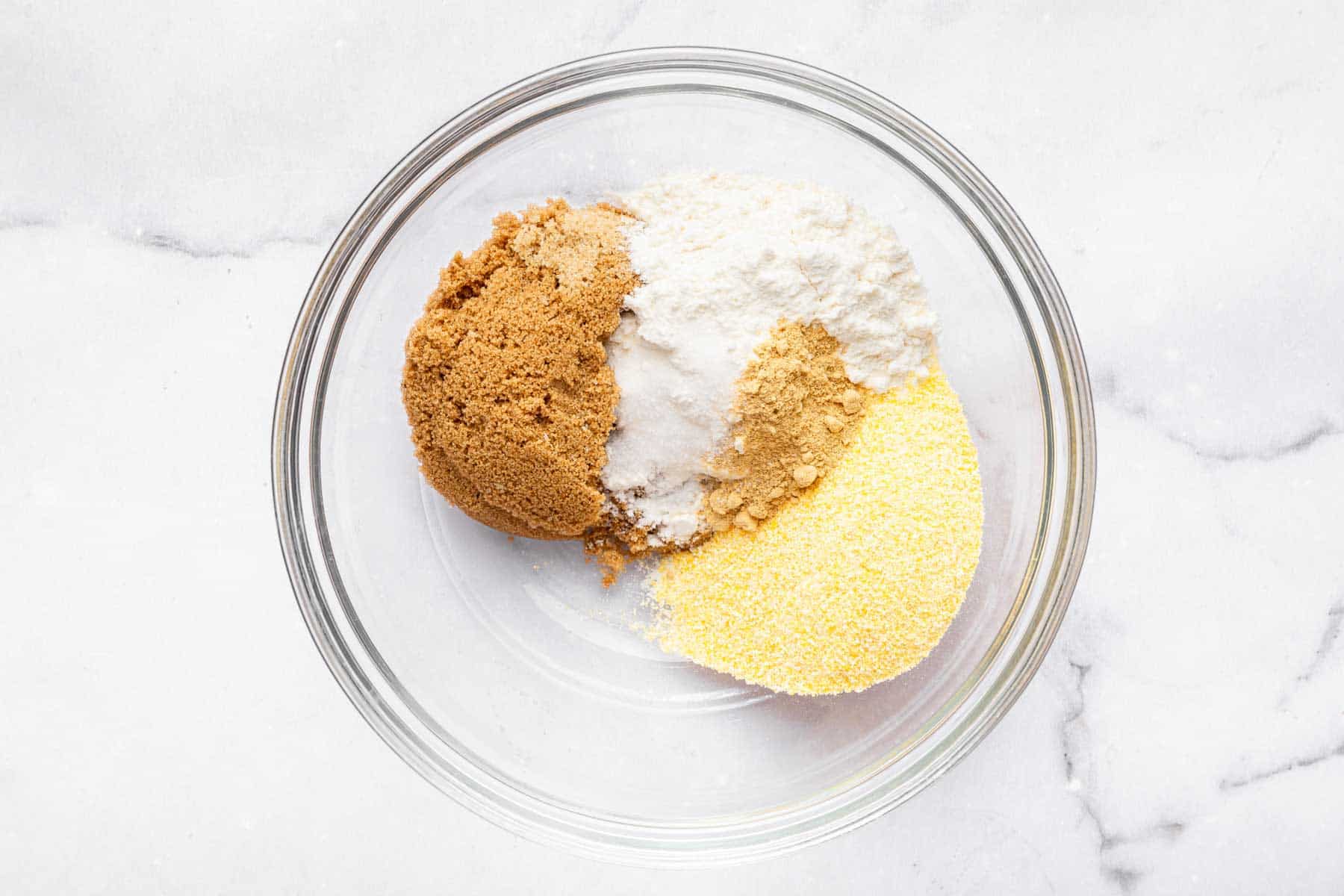 Clear glass bowl with brown sugar, cornmeal, and white powder.