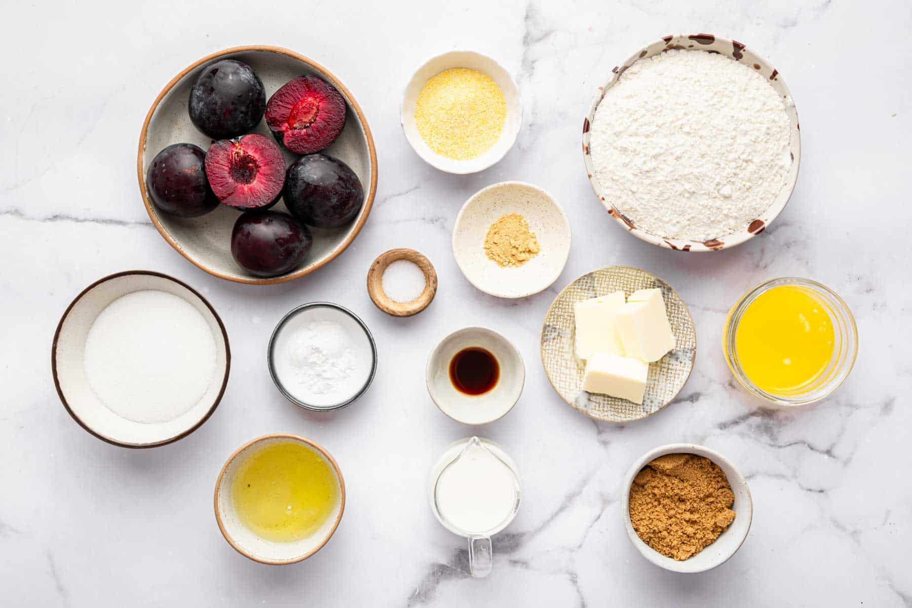 Bowl of fresh fruit, cornmeal, flour, melted butter, and brown sugar on kitchen counter.