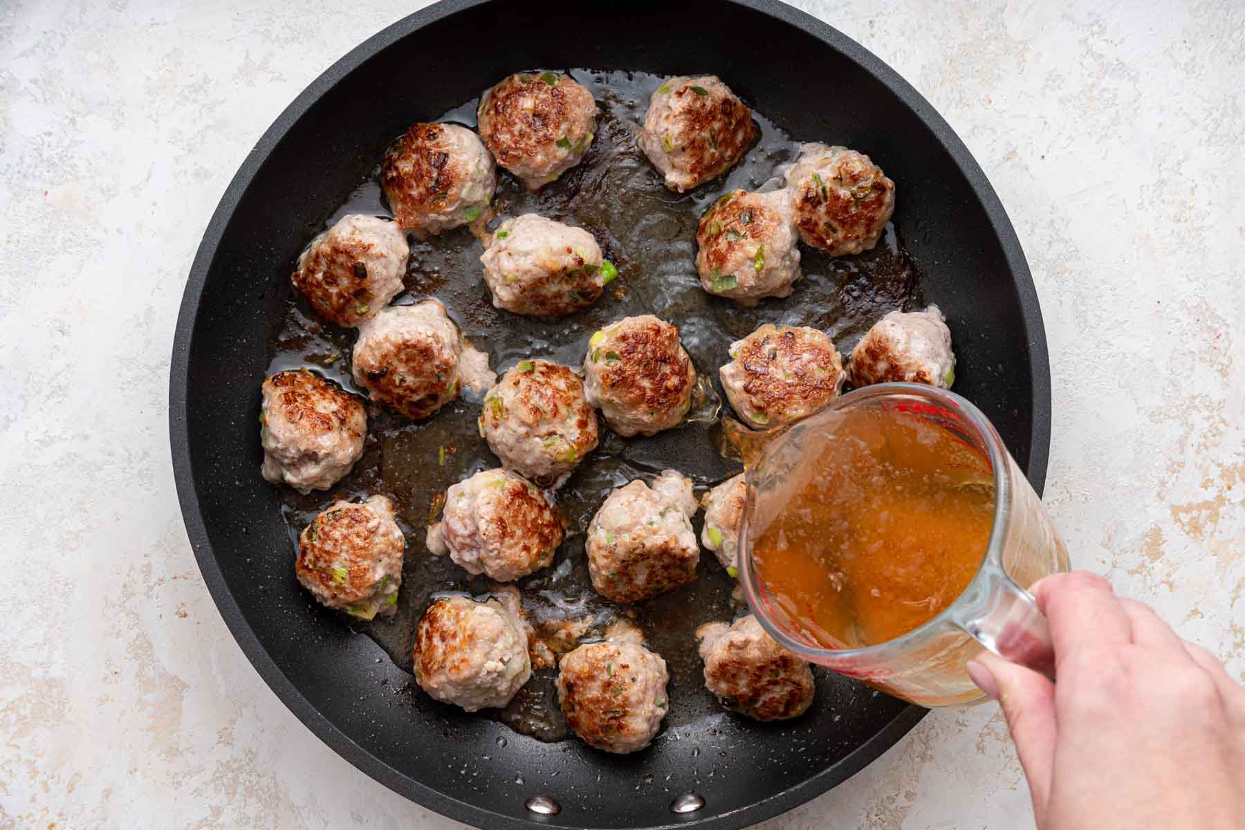 Pouring broth into a pan with browned meat in the bottom.
