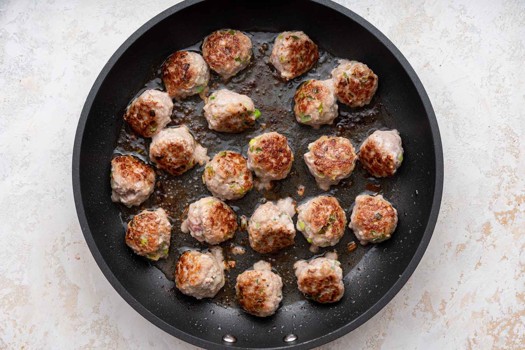 Meatballs browning in a cast iron skillet.