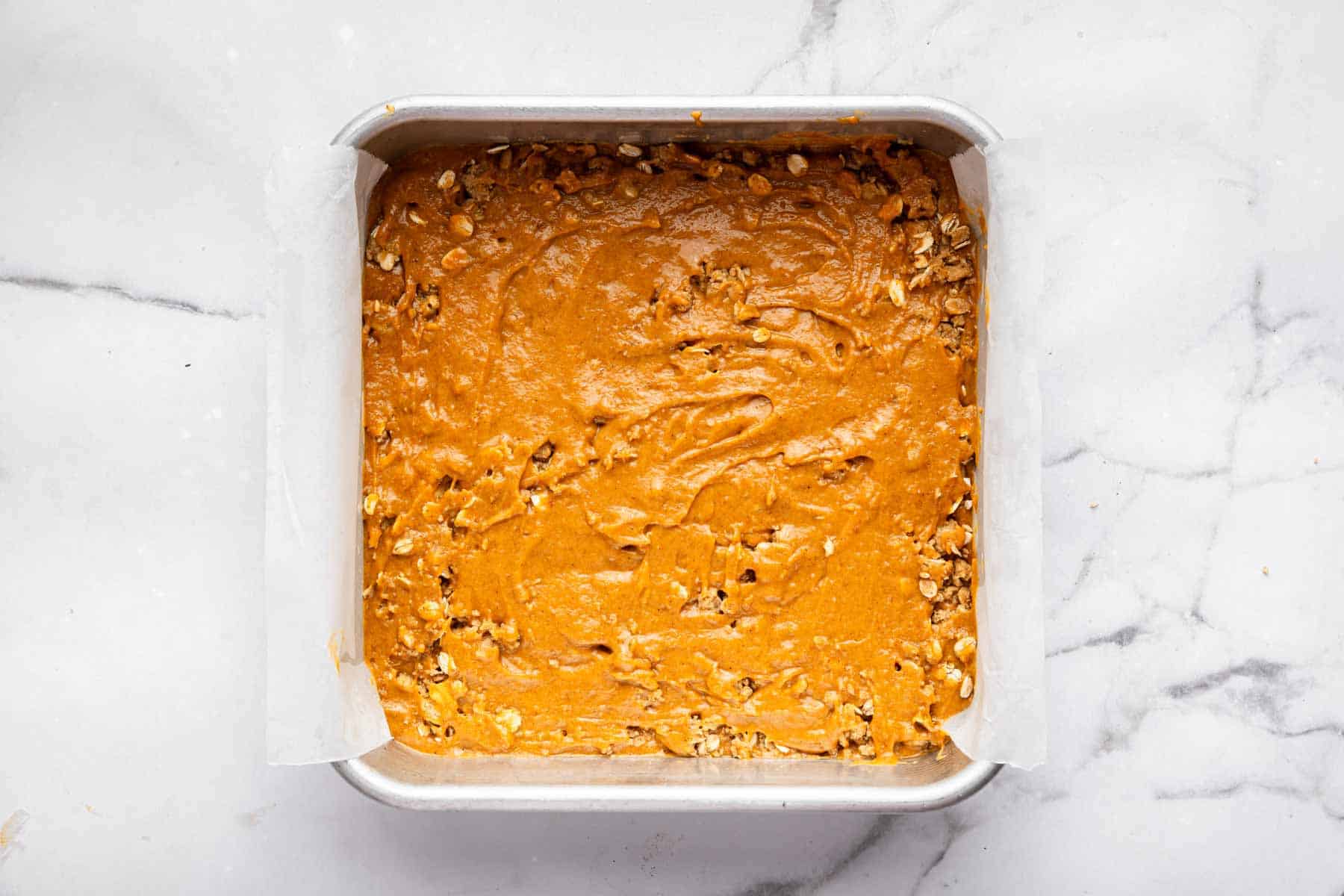 Orange batter in a square baking pan with oats peeking through.